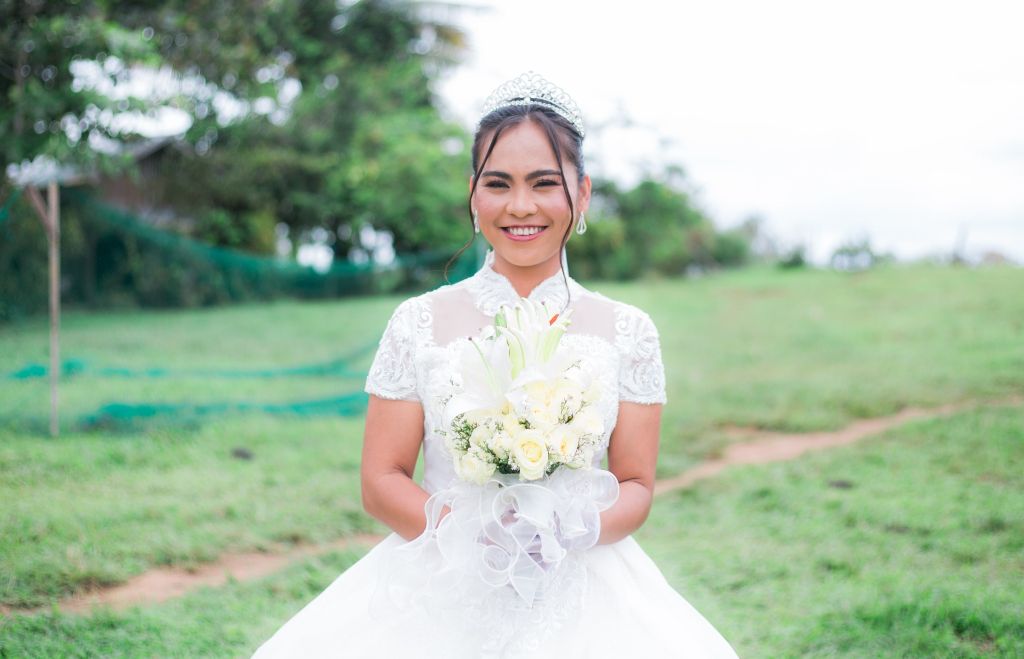 A proud Christian Filipina bride smiles on the grass while holding her bouquet