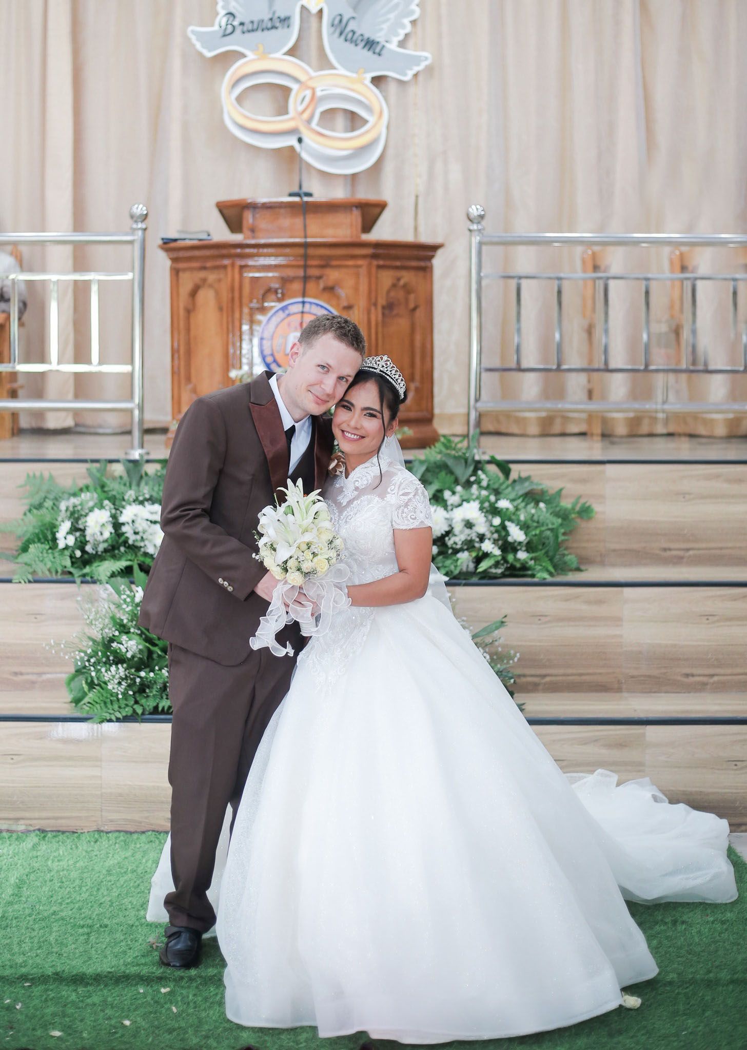 A groom and his bride hug in front of the church while posing for photos