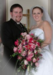 A wonderful Christian couple stand together in front of a cross, holding her wedding bouquet