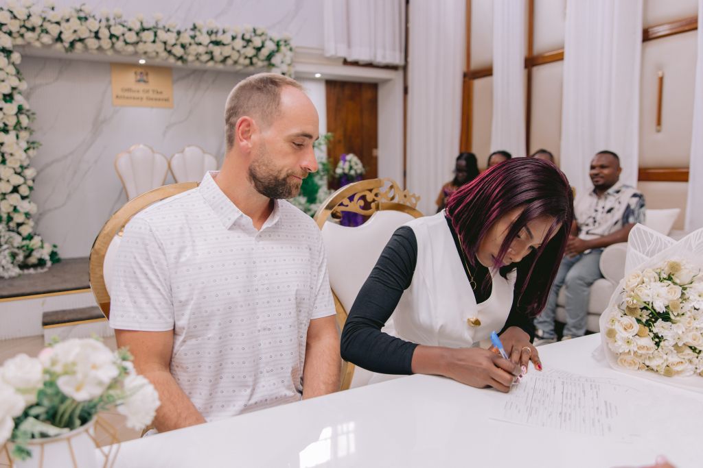 A new bride signs the register while her husband witnesses the signature
