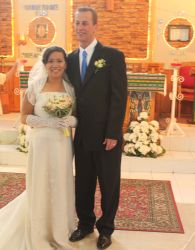 A tall White man stands next to his beautiful Asian wife, who smiles broadly