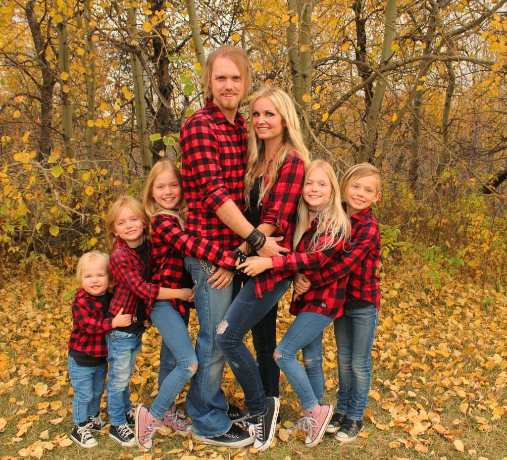 Family all dressed in lumberjack shirts smile in the cutest forest hug