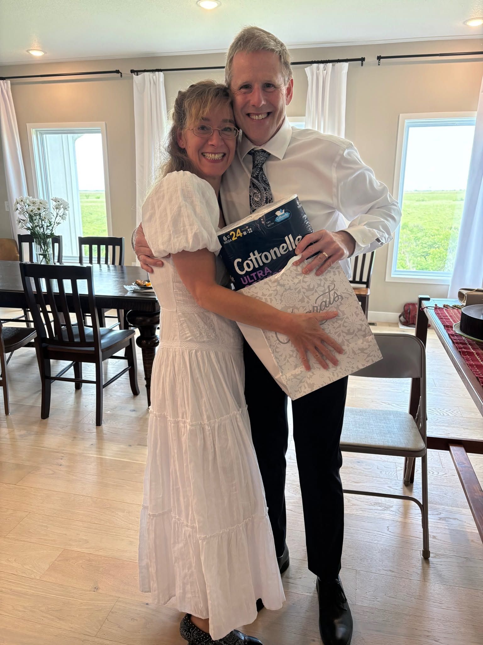 A well dressed couple burst out laughing as the man holds a gift bag containing some Cottonelle toilet paper