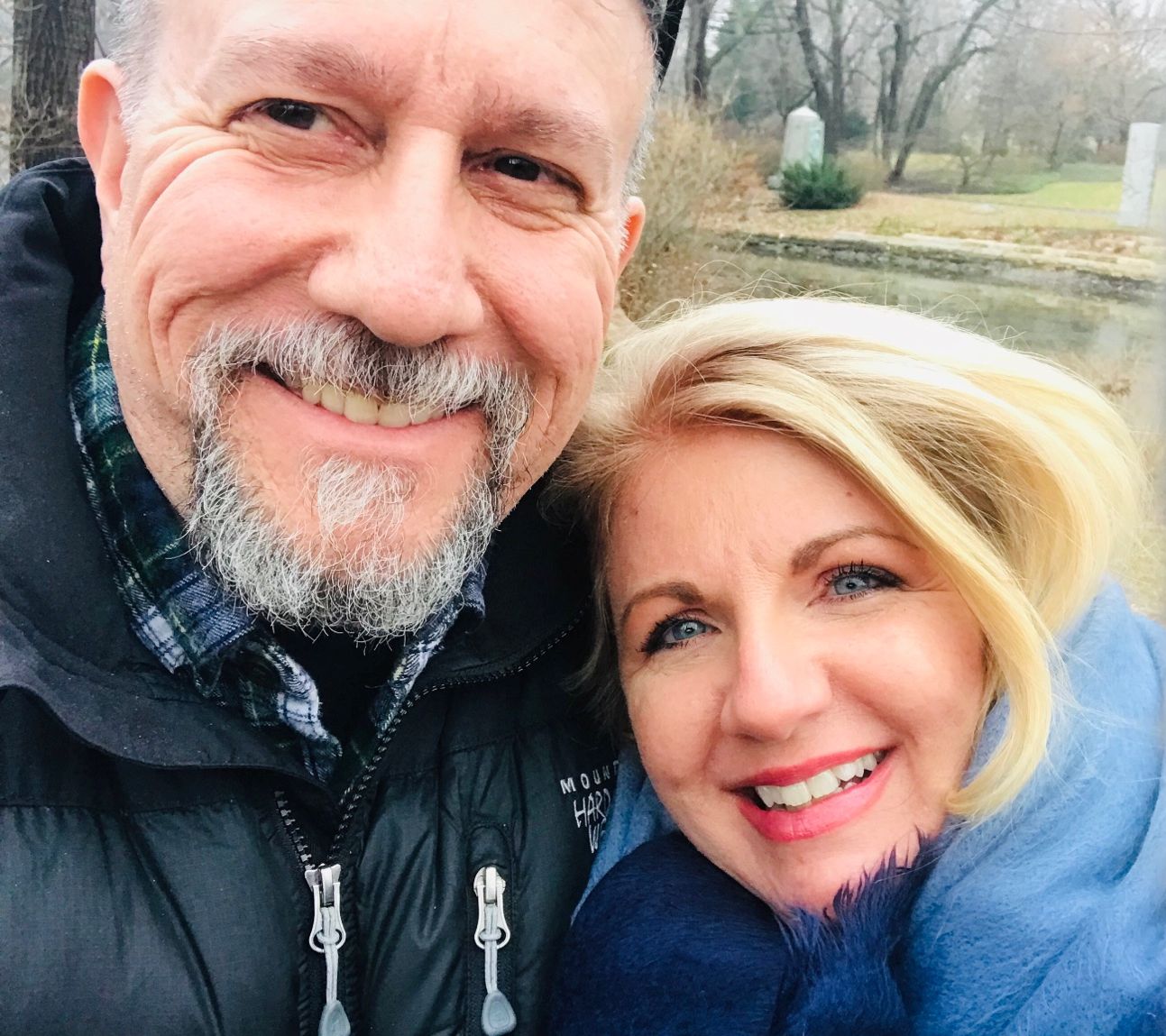A man in a goatee cuddles next to a woman with beautiful blue eyes, while out in the cold together