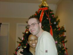 A pretty Black Christian woman smiles and hugs her new love in front of a Christmas tree