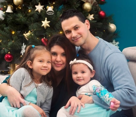 Proud Christian parents sit in front of Christmas tree with 2 daughters