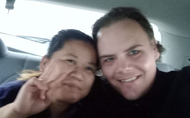 An Asian woman flashes a peace sign as she leans into her White husband, as they smile in the back of a car