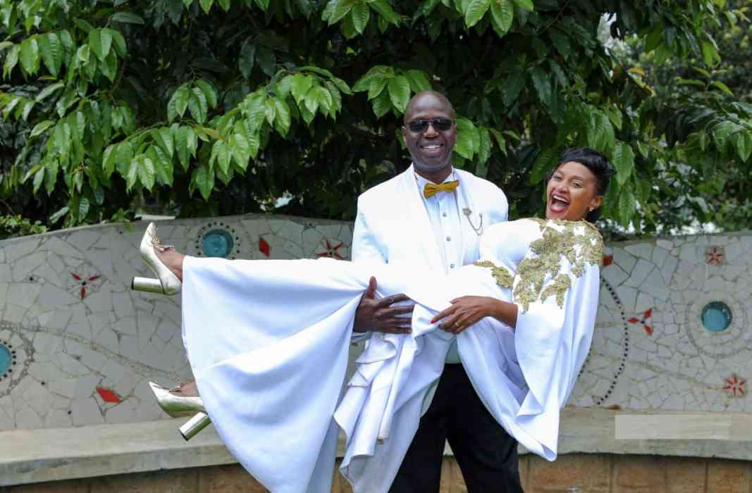 Kenya Christian groom in white carrying his Kenyan bride as she laughs