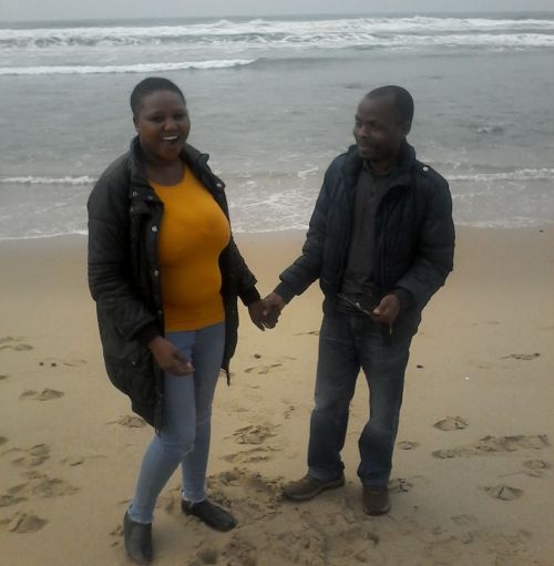 South African standing on beach laughing while holding Malawi fiances hand