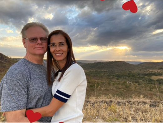 A tall Brazilian woman in glasses hugs a Texas man in glasses in a field at sunset
