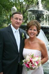 Southern Christian widower stands next to his beautiful new bride in front of a fountain