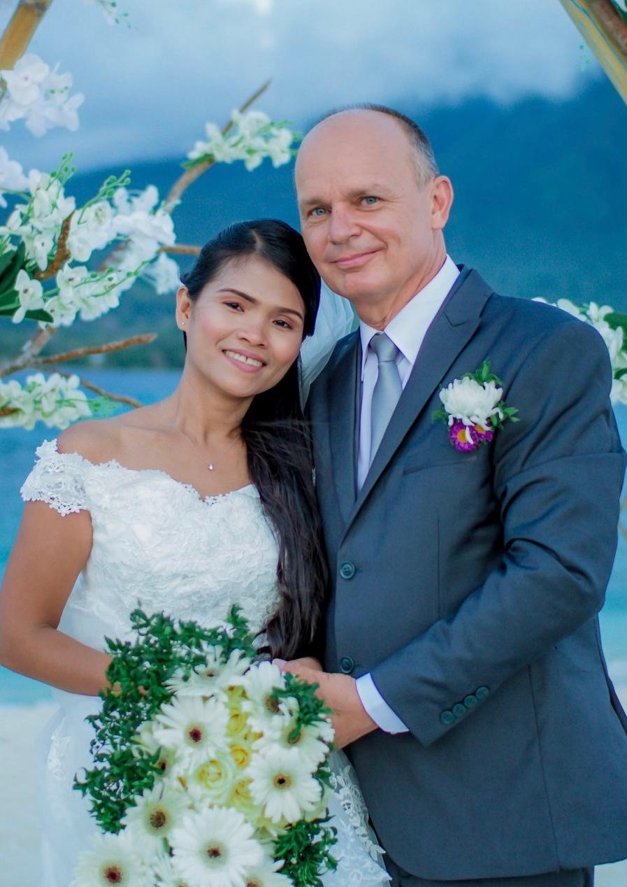 Very happy White man stands next to his East Asian bride who holds bouquet