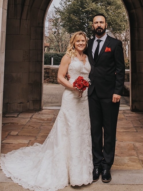 A Christian couple pose on their wedding day in front of a stone archway