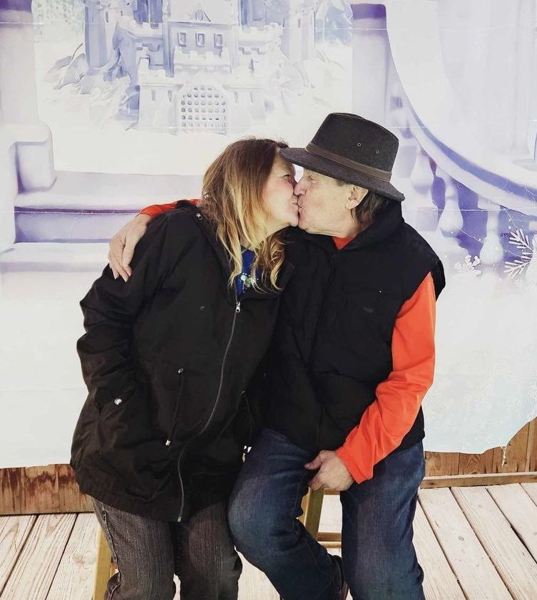 A mature Christian couple kiss in front of a Christmas wonderland scene