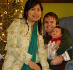 Happy Christian couple with their new baby cuddle on the couch in front of Christmas tree