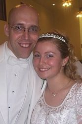 A happy smiling man in a white suit stands next to a beautiful woman in a tiara