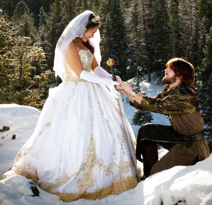 A man on bended knee presents a flower in the snow to his beautiful bride in a white dress