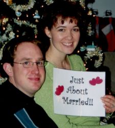 Christian singles sit together and smile while holding up a Just About Married sign