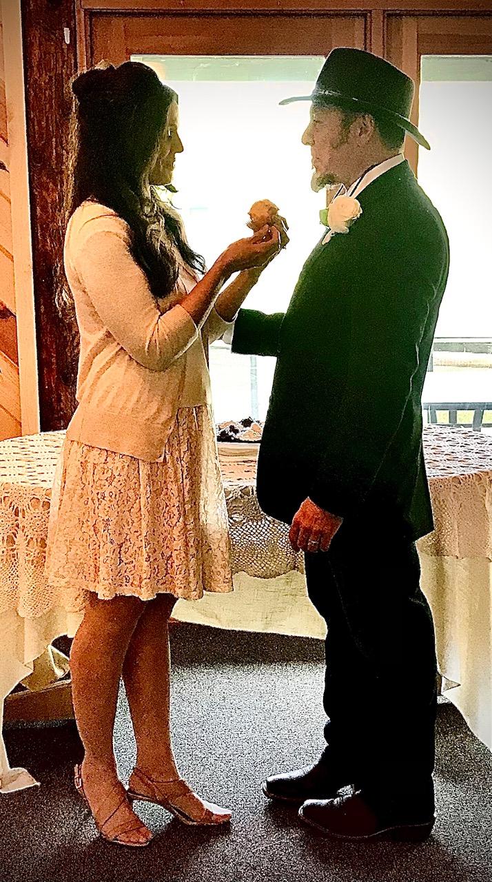 A beautiful woman in a lace white skirt pins a boutonniere in a man wearing a black suit and black hat