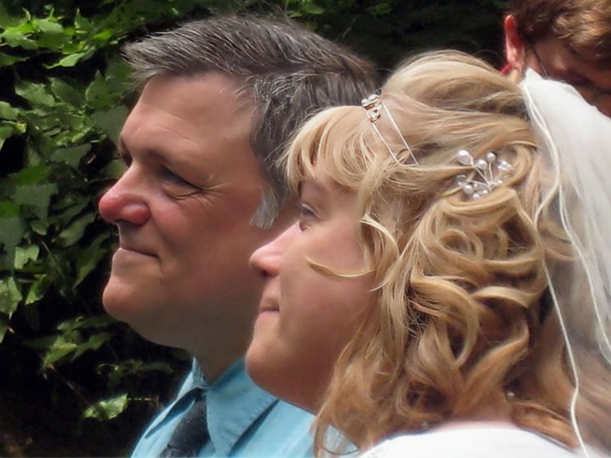 A mature Christian couple receive a blessing on their wedding day outdoors.