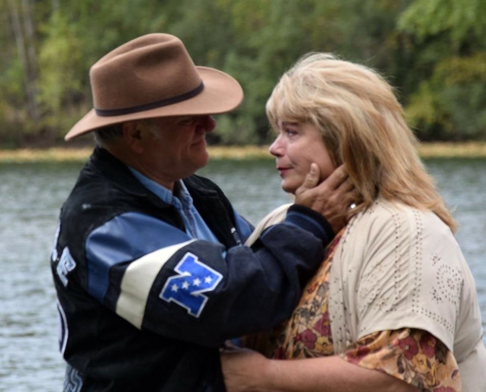 A man in a cowboy hat tenderly consoles his wife who stands by the water with tears in her eyes