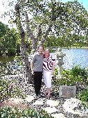 A man hugs a woman in a garden by a lake