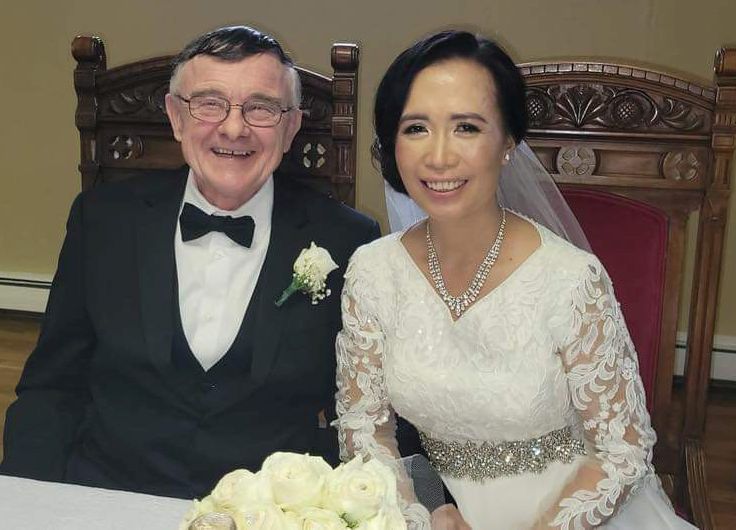 An older interracial couple share a laugh as they pose for wedding photos while seated