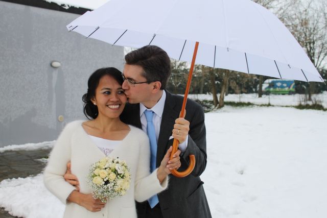 Man sneaks a kiss while under an umbrella with a beautiful woman