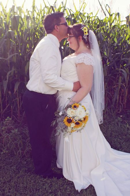 Tender moment when groom kisses his beautiful wife tenderly on the head while outdoors next to corn field