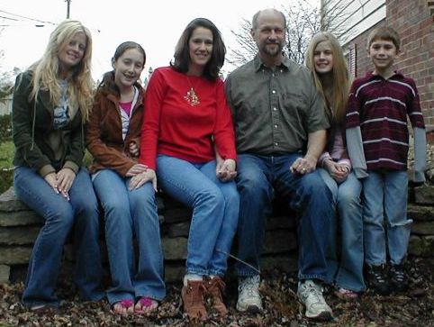 Blended Christian family hold hands and pose outside their house