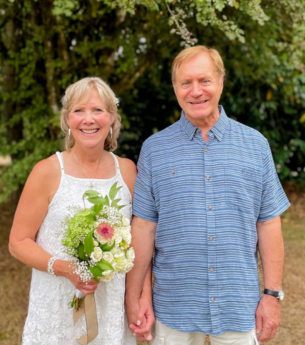 A joyful bride holds her new husband's hand as she holds beautiful bouquet of flowers outdoors