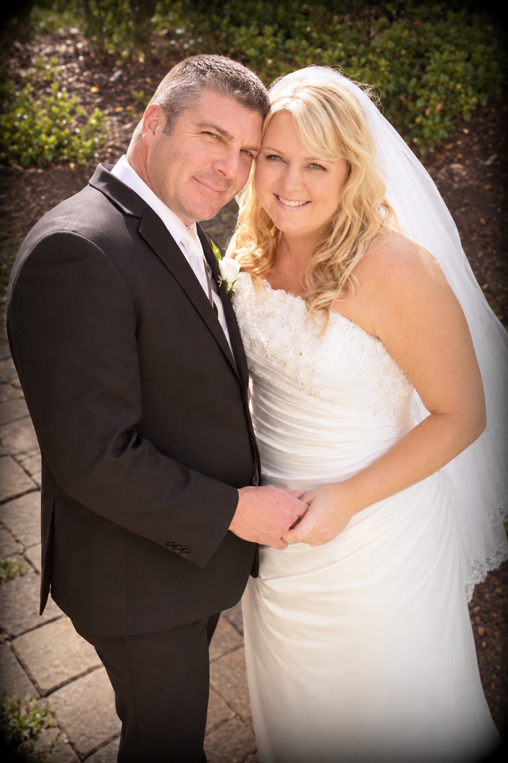 A NZ woman looks radiant at sun shines through her hair and she smiles and holds hands with her Australian husband