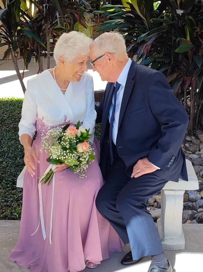 Senior Christians nuzzle while sitting on a bench after marrying