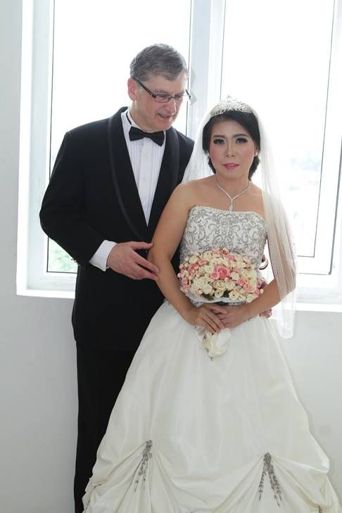 Madly in love White man tenderly talks to his beautiful Asian bride who holds bridal bouquet
