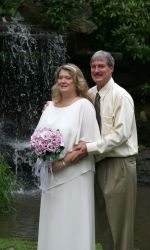 A man lovingly holds his wife from behind, with a waterfall in the background