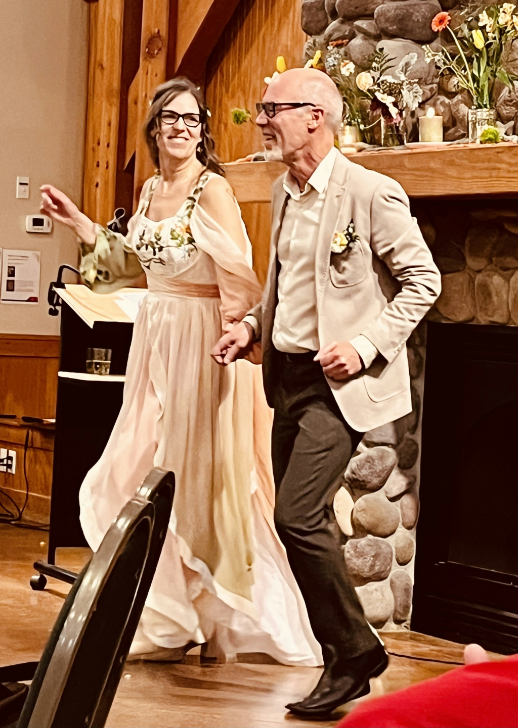 A bride and groom dance while laughing in front of a fireplace at their reception
