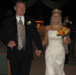 A beautiful bride holding flowers in one hand and her lucky husband in the other smiles