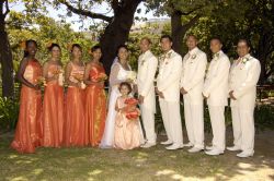 Bridesmaids in orange and groomsmen in white flank the happy married couple