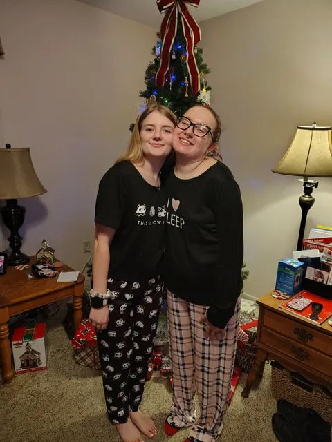 Adult sisters smile while pose together in front of a Christmas tree