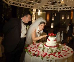 A bride playfully tries cutting the wedding cake with her finger while the groom laughs