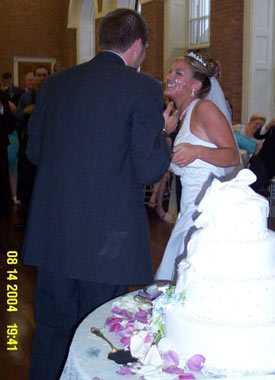 Laughing bride tries in vain to avoid getting wedding cake on her face