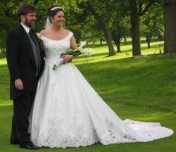 A pretty Christian bride in a beautiful wedding dress poses on the grass with her new Christian husband