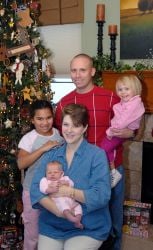 Christian parents pose by the Christmas tree holding their 3 children