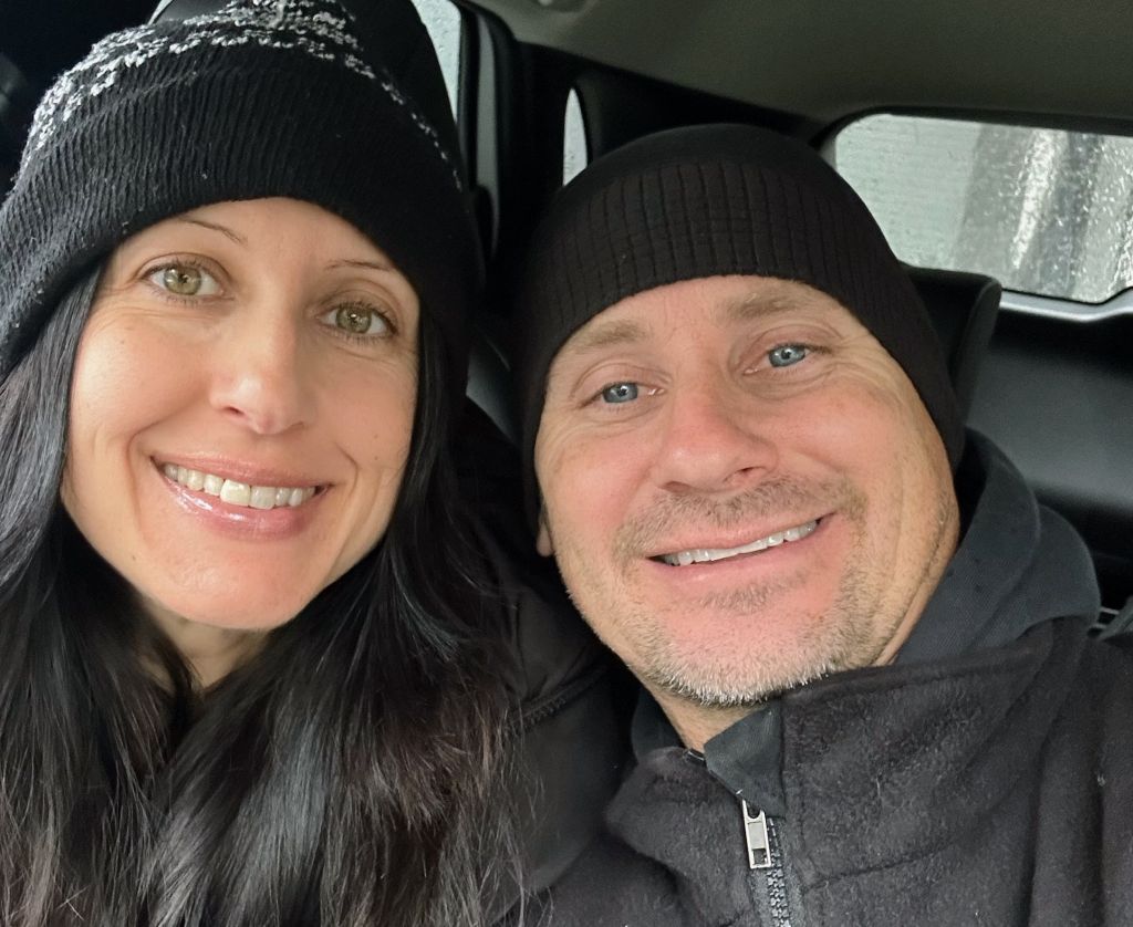 A couple wearing toques take a selfie in their car
