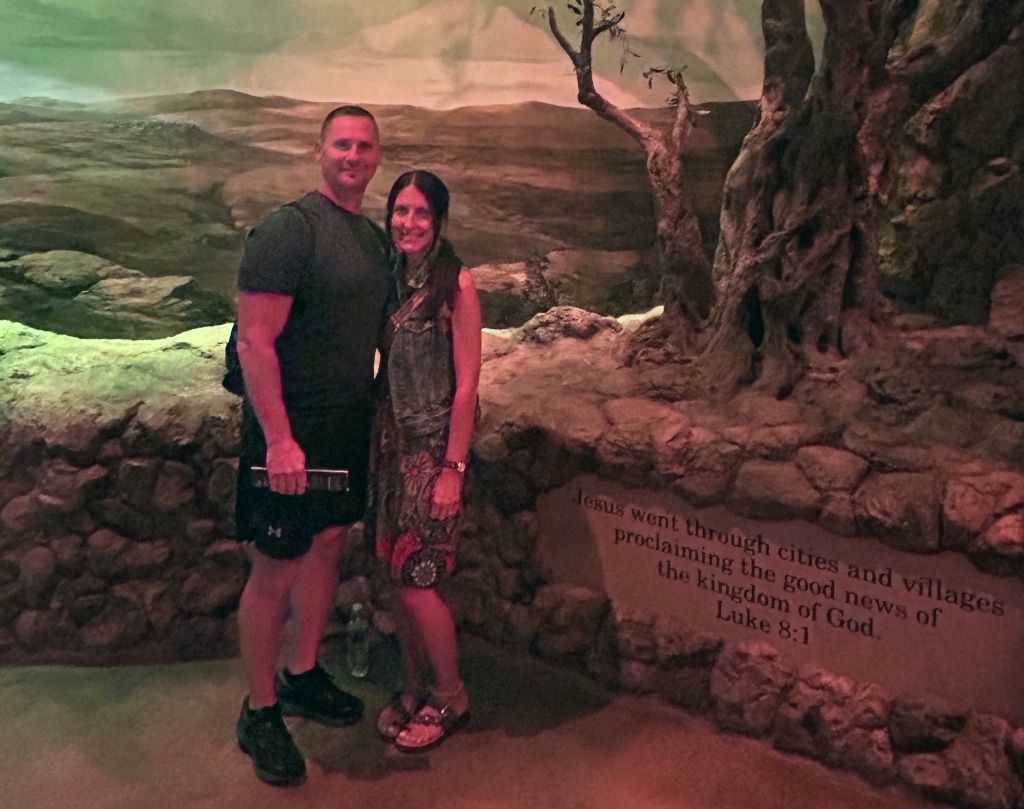 A Christian couple stand next to a sign which contains a verse from the book of Luke