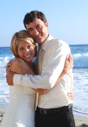 A man hugs a woman in a tight embrace while she looks overjoyed at the beach