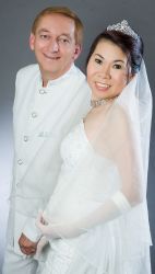 A happy new bride smiles next to her elated husband, both dressed in white