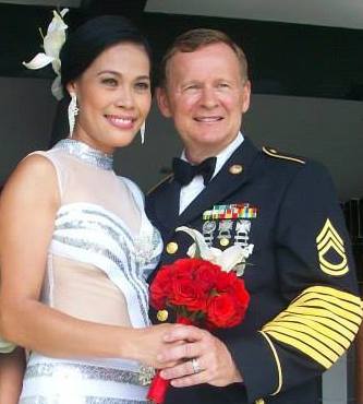 A gorgeous Asian woman holds a red bouquet of flowers while standing next to a good looking White man in military suit