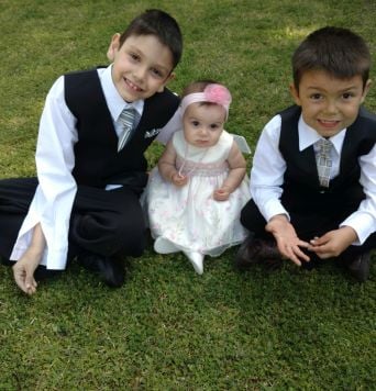 Adorable brothers in suits hug baby sister on grass