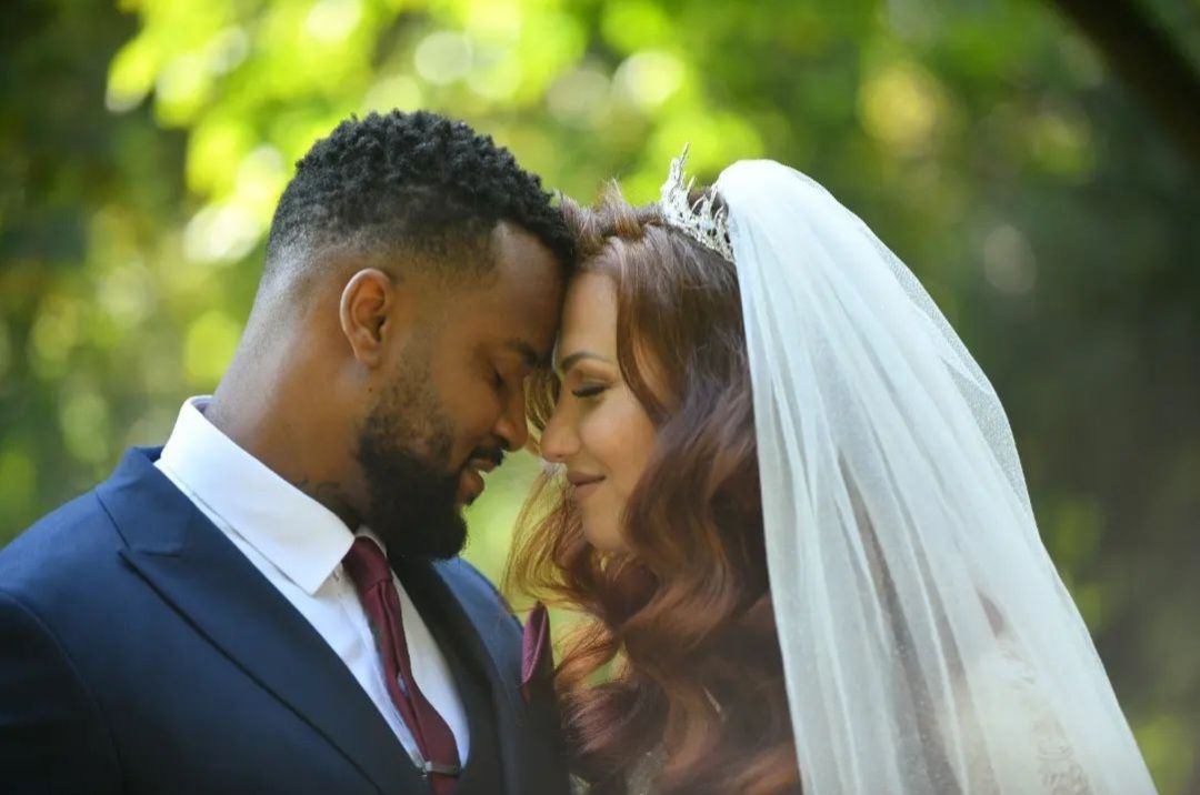 A beautiful White bride and her Black husband touch their heads together in joy on their wedding day outdoors